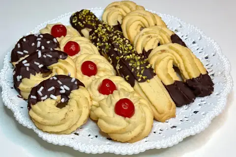 Vassoio di frolla montata: biscotti decorati con cioccolato, granella di pistacchio e ciliegie candite.